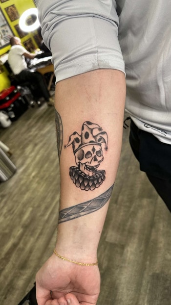Jester Skull Tattoo By Choze, an artist at Iron Palm Tattoos In Downtown Atlanta GA. The jester skull tattoo can be seen as a reminder of the fragility of life and the inevitability of death. It can also represent the duality of life and death, joy, sorrow, comedy, and tragedy. It can also be a symbol of irony reminding us that even those who bring joy and laughter can experience the same fate as anyone else. Call 404-973-7828 or visit for a free consultation with a body artist. Walk Ins are welcome.