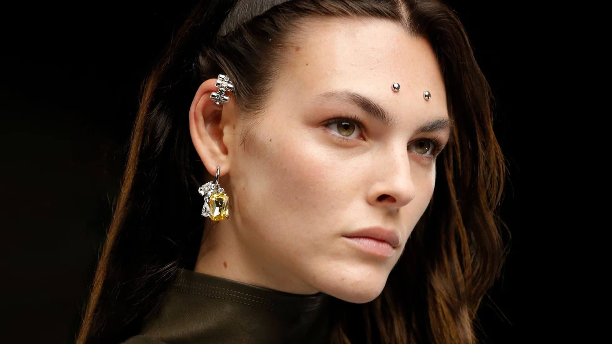 Close-up of a model with forehead dermal piercings showcasing multiple small silver studs on the forehead and additional ear piercings