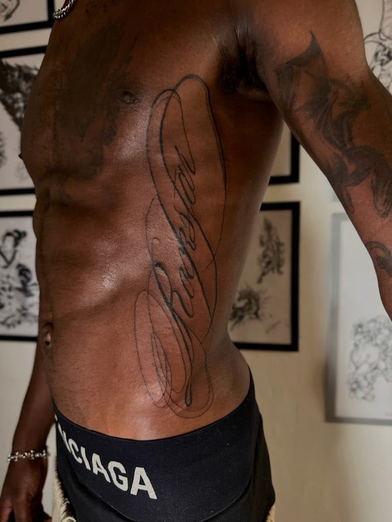 Fine line script tattoo with long flowing cursive lettering across the ribcage